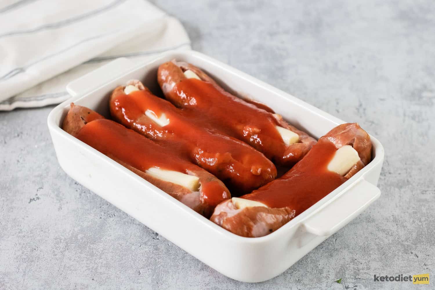 Italian sausages stuffed with mozzarella cheese sticks and marinara sauce in a baking pan